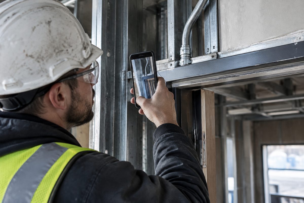 Worker photographing a conduit junction above unfinished door framing